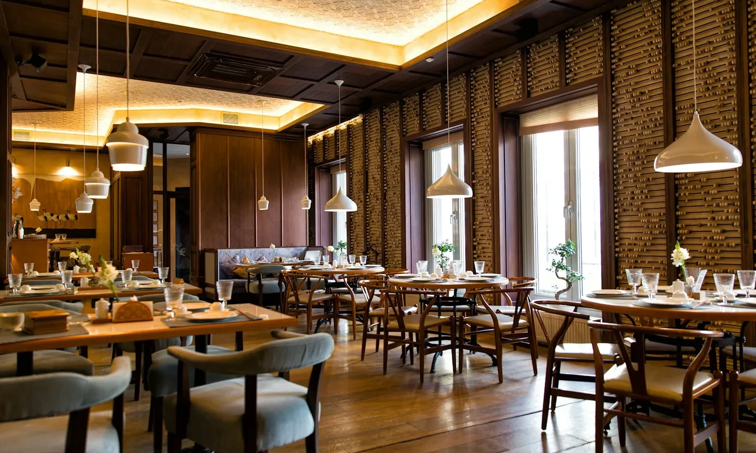 Salle de restaurant dressée, tables en bois et suspensions blanches